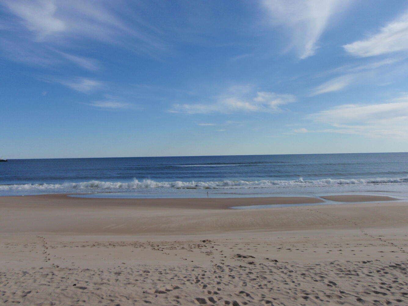 A calm sea with waves flowing onto the sand, forming a sandbar at the base of the beach