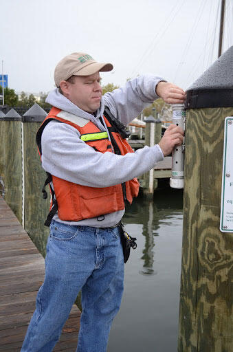 A man removes a plastic tube from a wooden post at a dock.