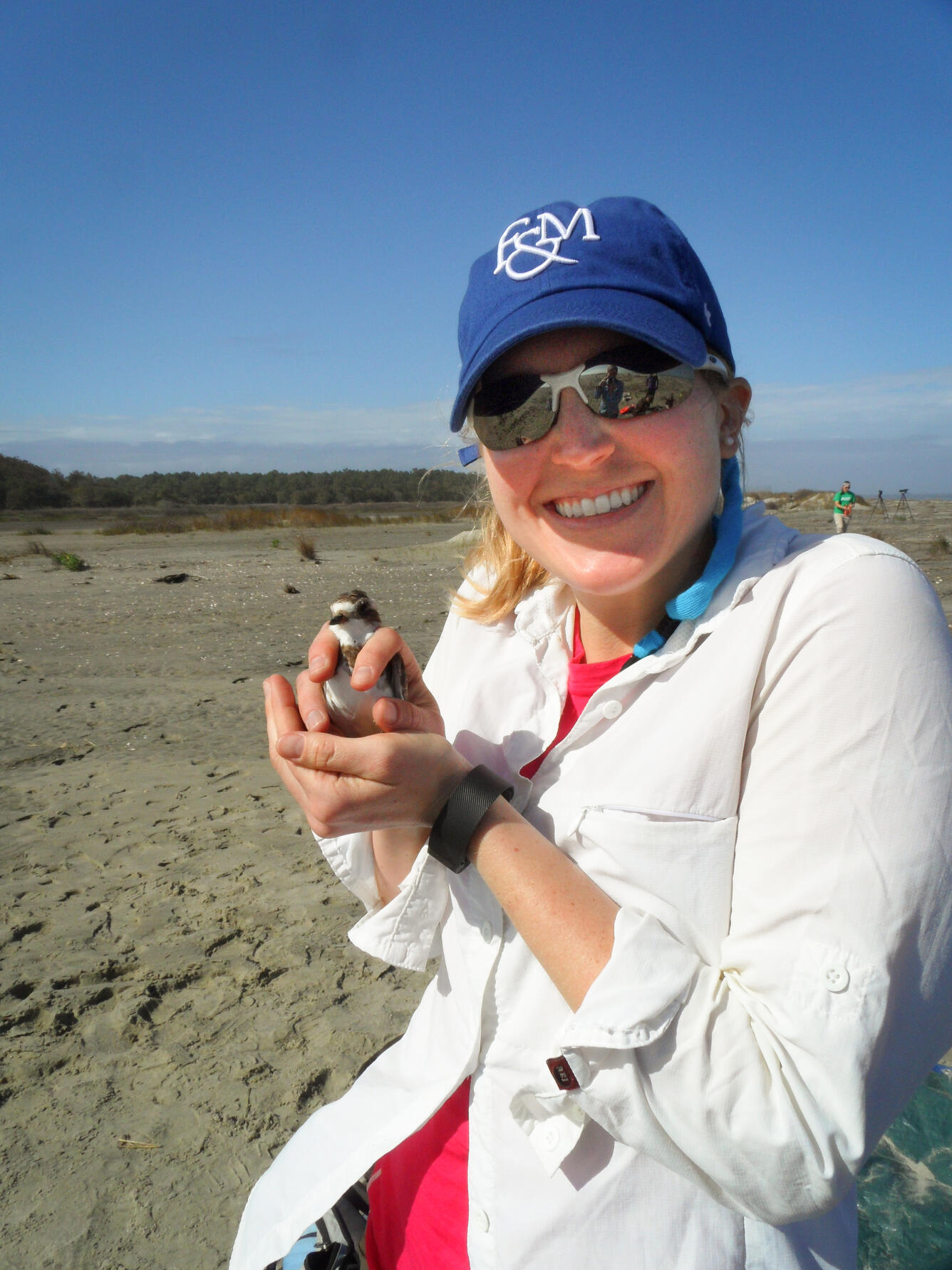 A woman holding a small shorebird while standing on a beach