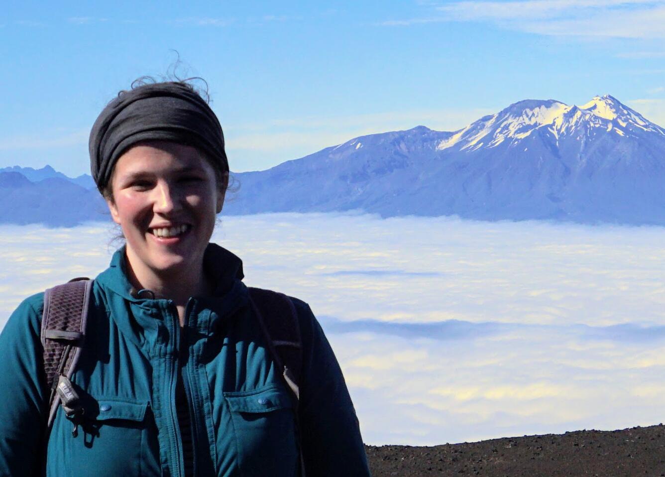 Woman standing with clouds and a volcano in the background.