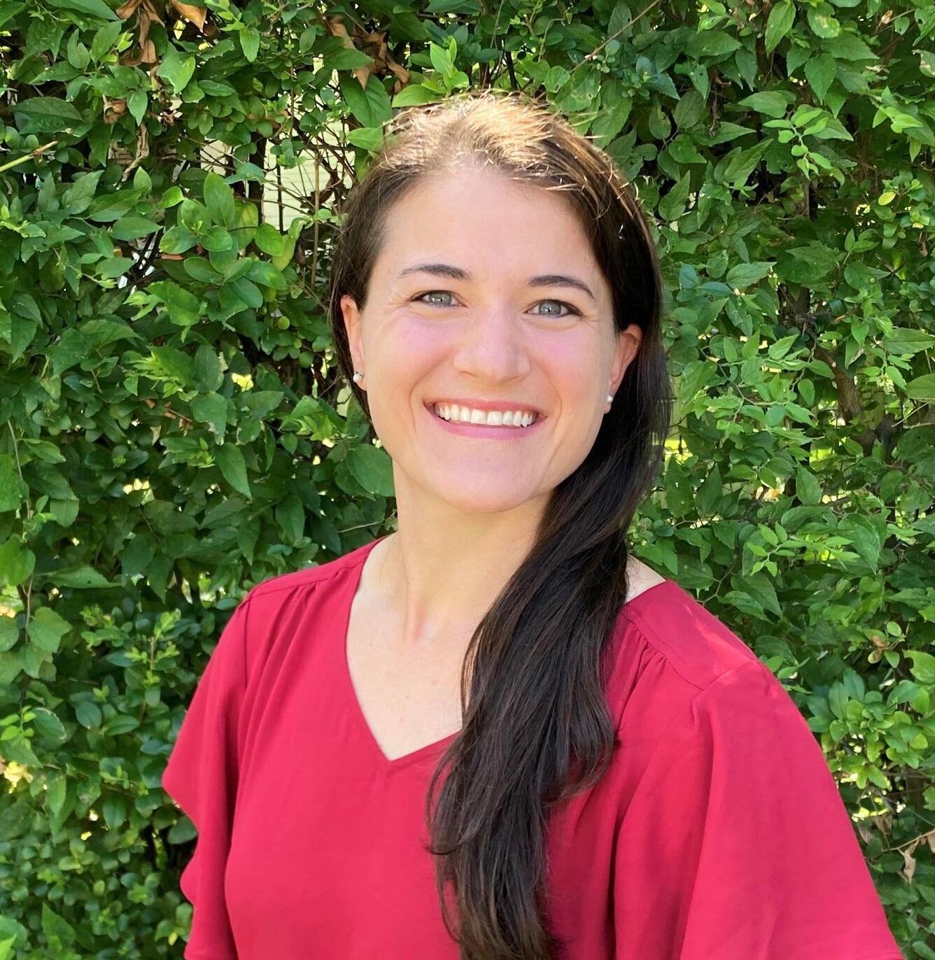Woman in red shirt standing against bush