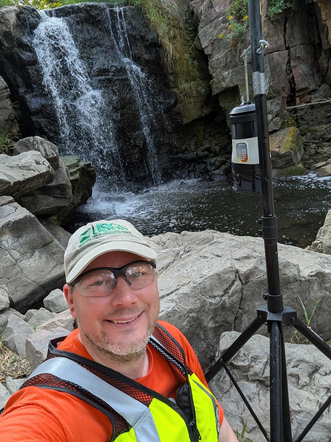 Scientist standing next to air sampling equipment with waterfall in background