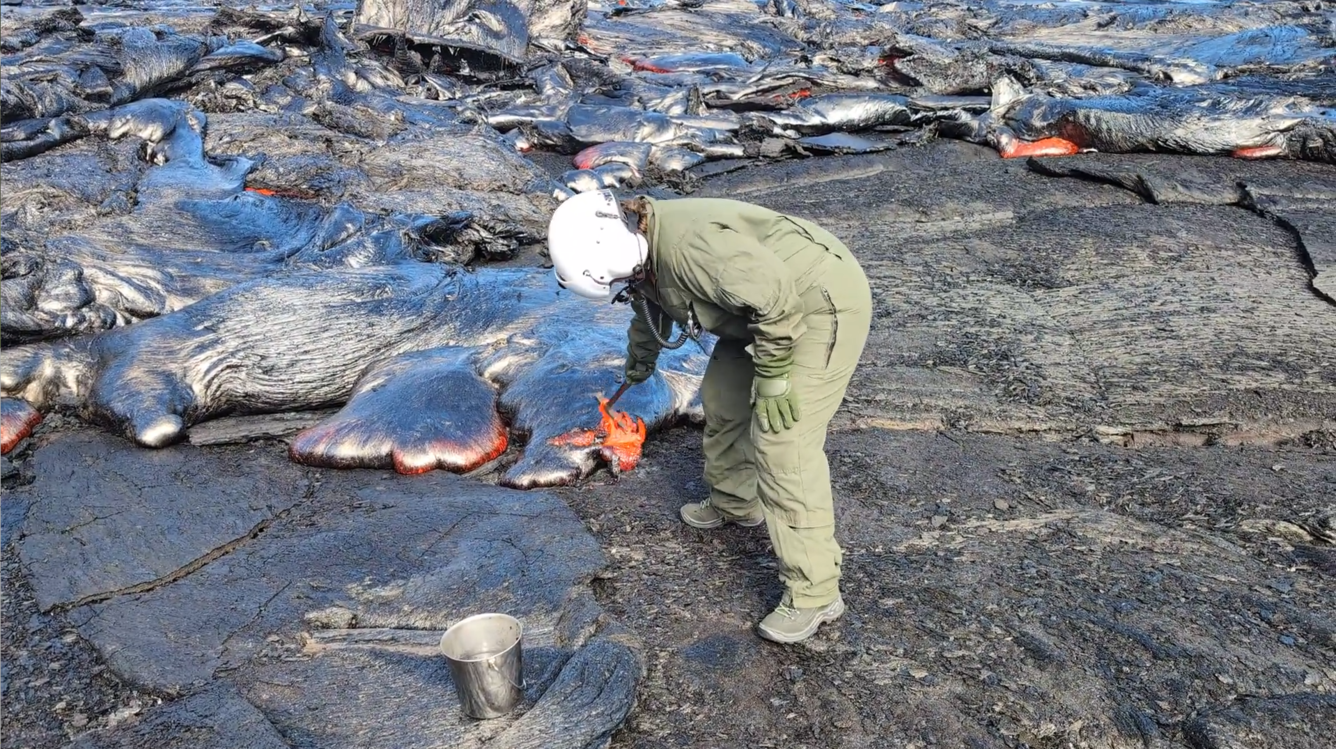 Color photograph of scientist collecting sample of lava