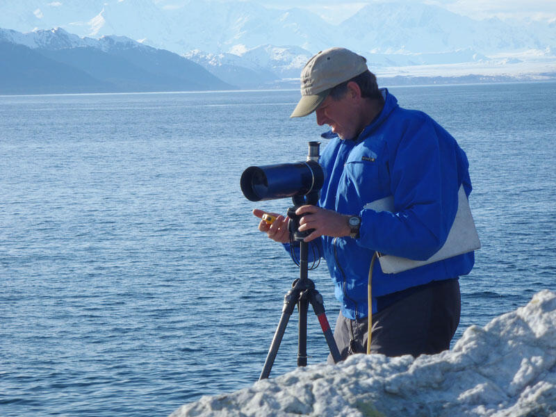 A man stands near a camera on a tripod stand looking at a stopwatch.