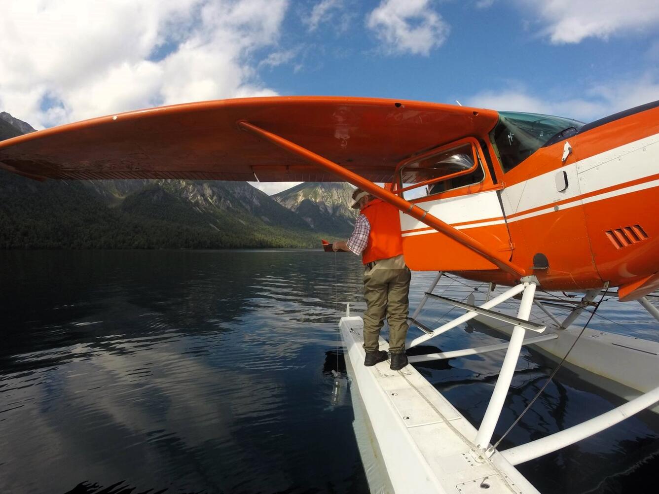 A scientist stands on a seaplane float and collects a water sample from a lake