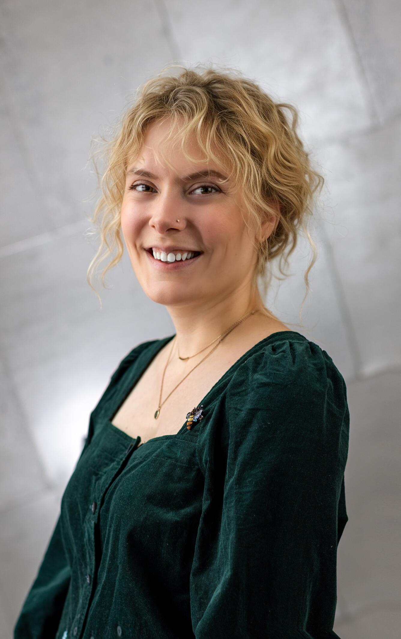 A woman with blonde hair and a green blouse smiles for her picture.