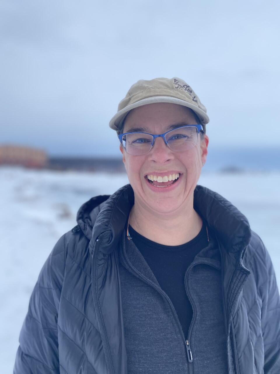 Smiling woman wearing glasses and hat with snowy background