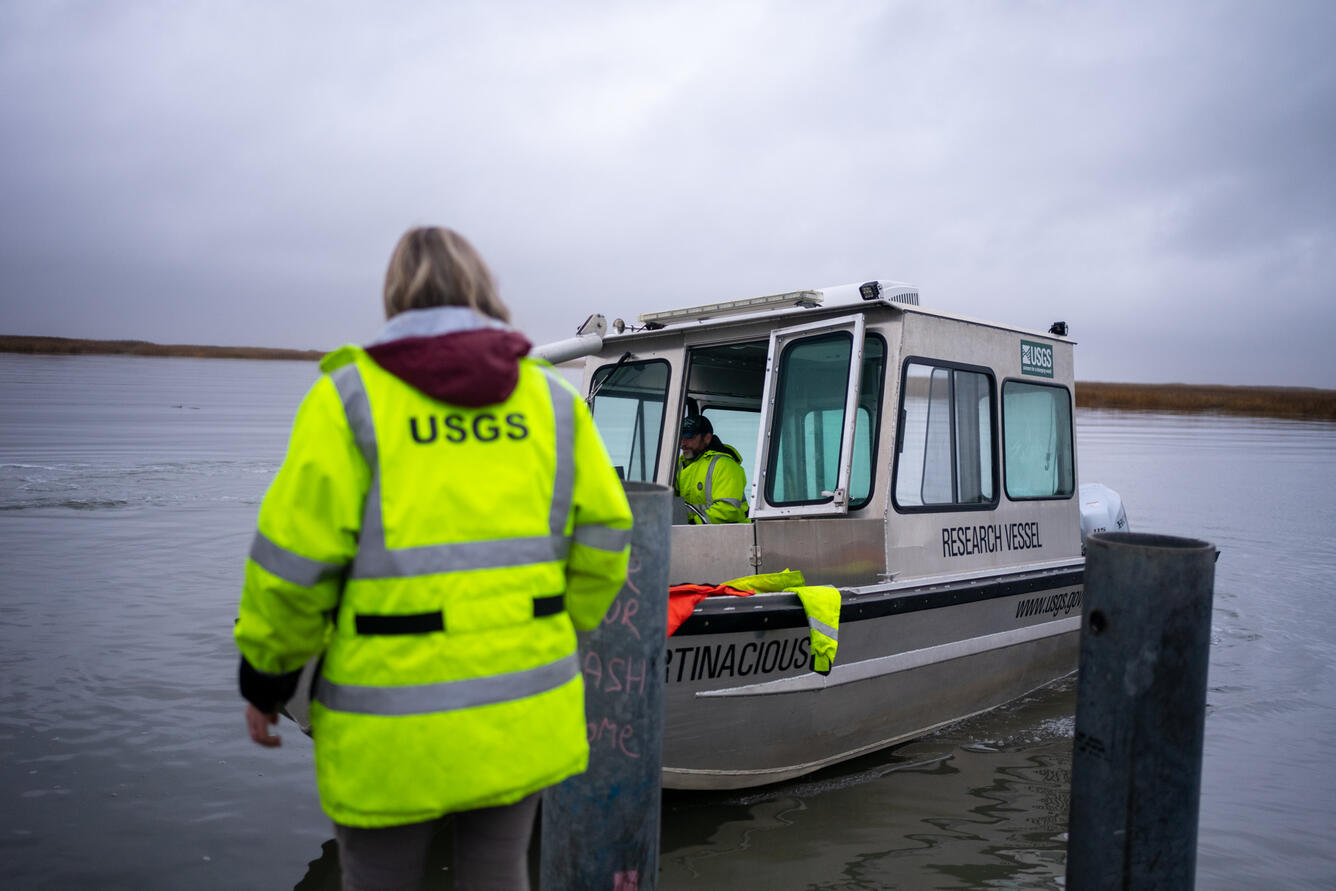 A person guides a boat to a dock as another looks on.