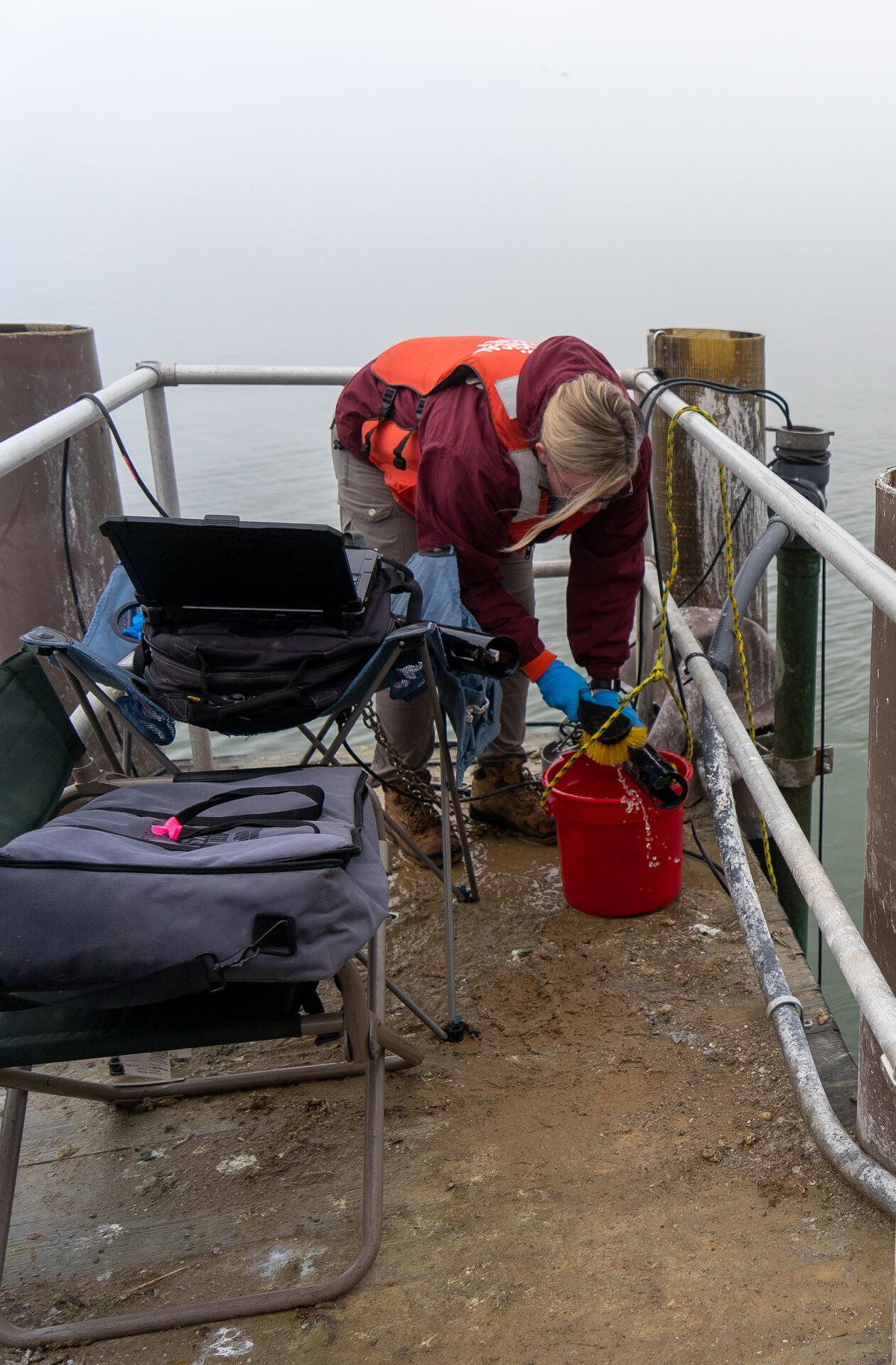On a dock, a person uses a brush to clean a sonde.