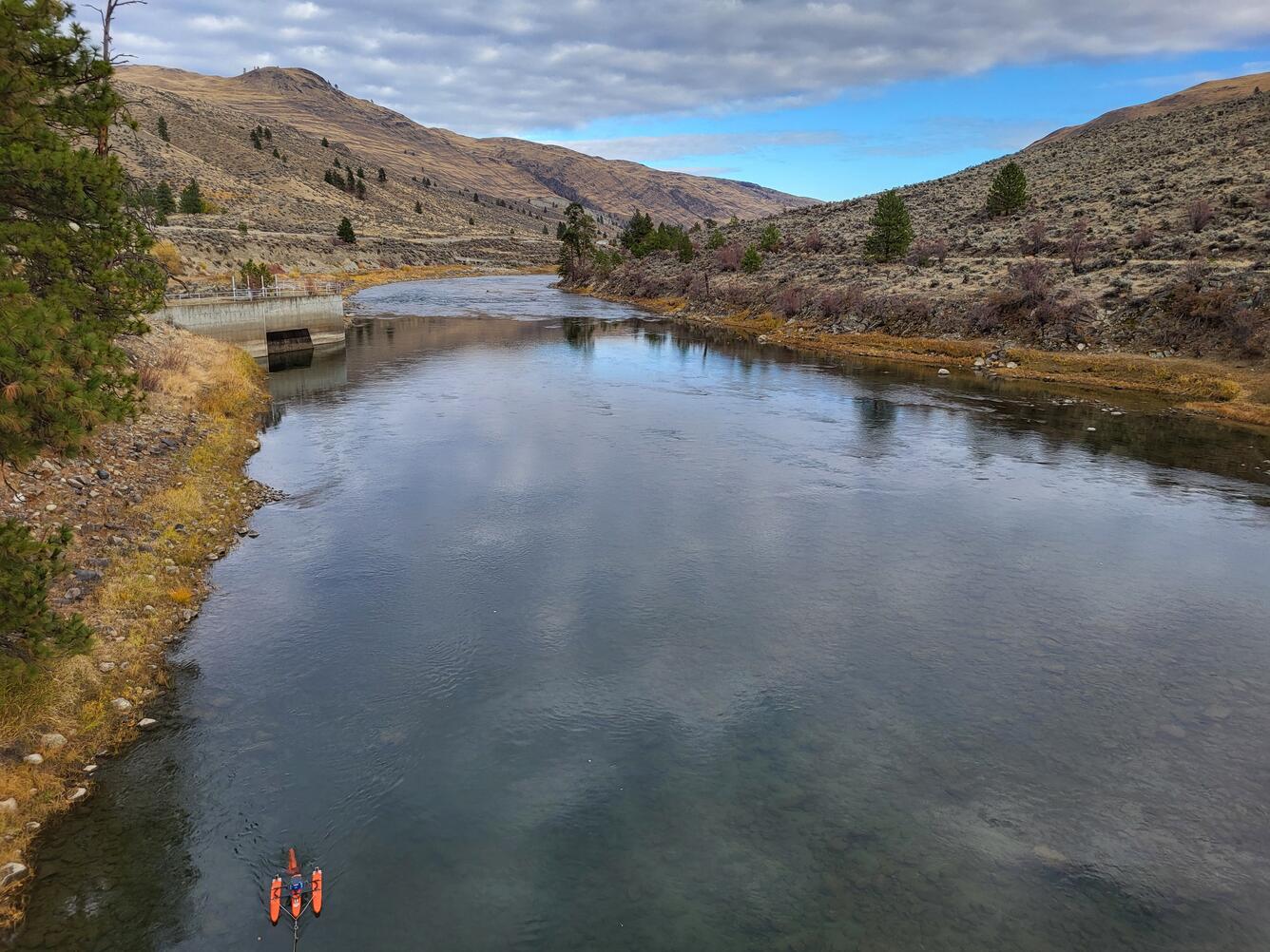 Small boat floats in river with dry grassy hills in background