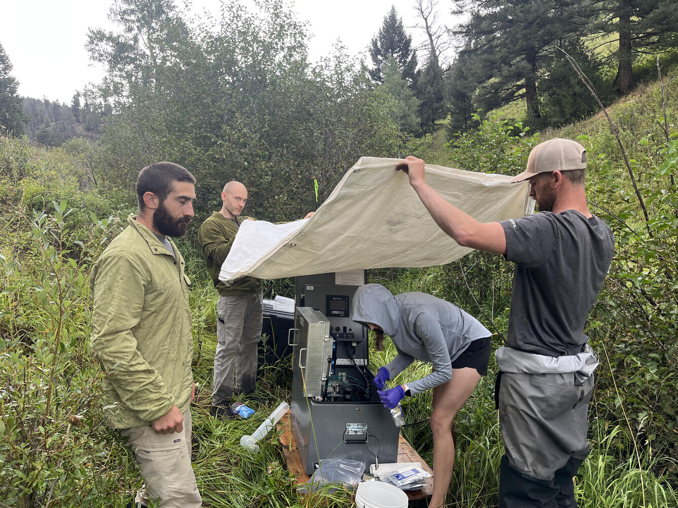 Four people help install an automated stream sampler in the rain