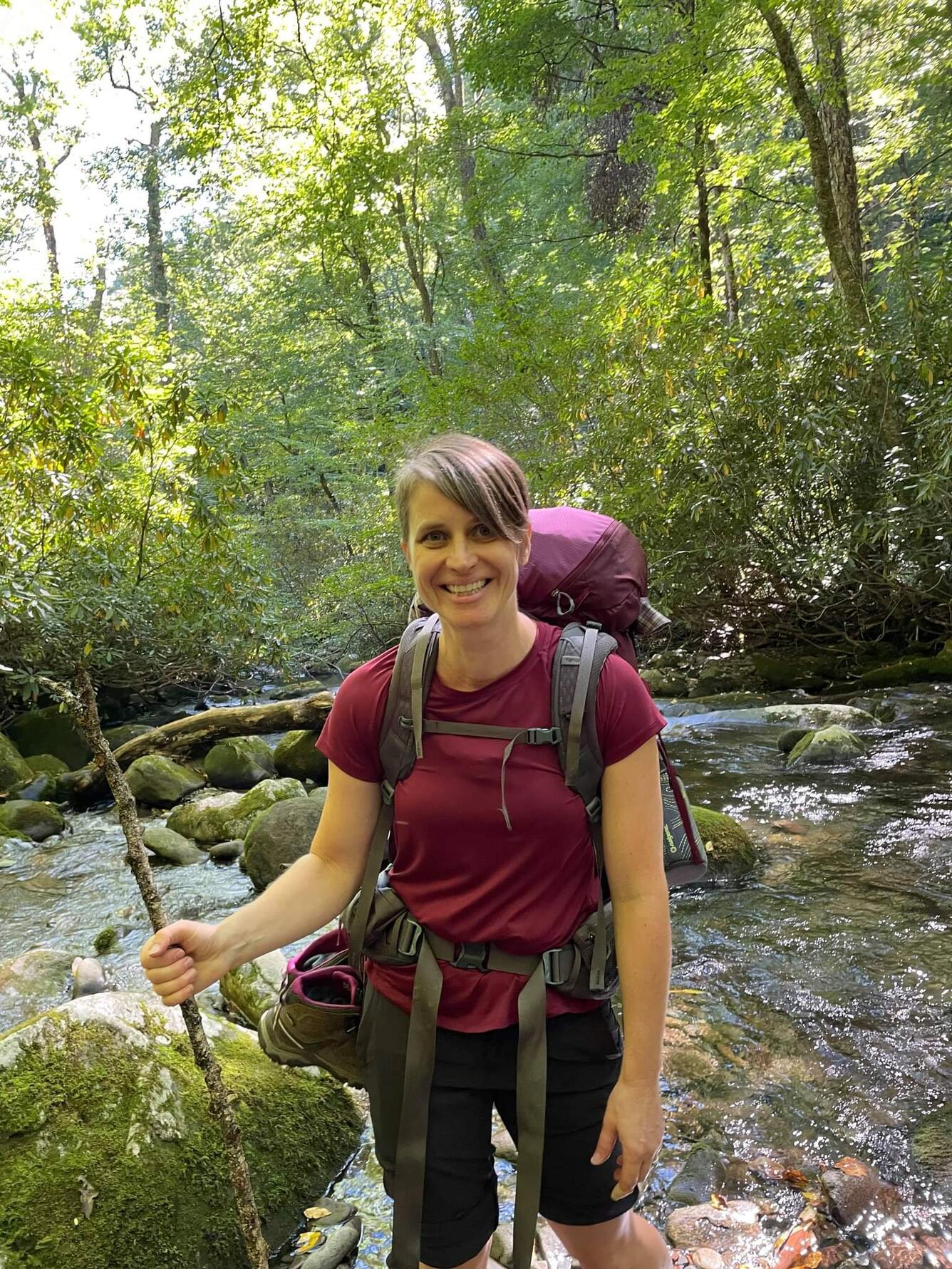Woman with backpack hiking in forest near stream.