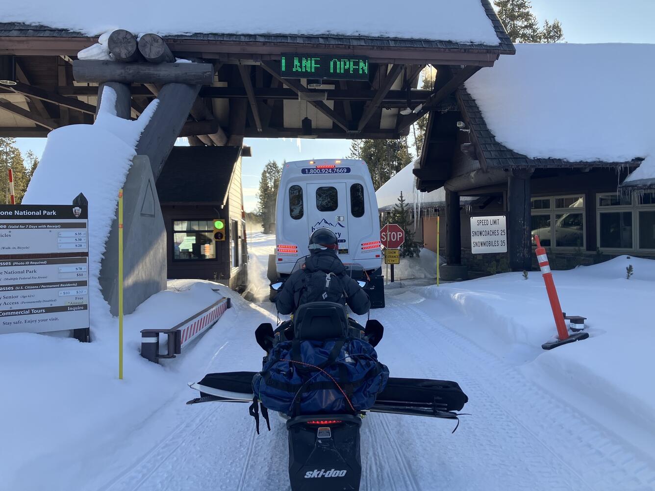 A person on a snowmobile waits behind an oversnow van at the park entrance station 