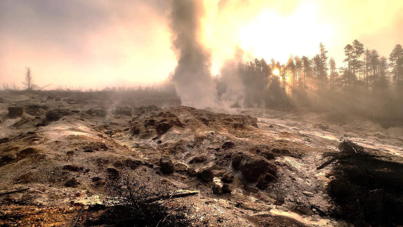 Steam rising in the distance over a rock slope as the sun rises in the background
