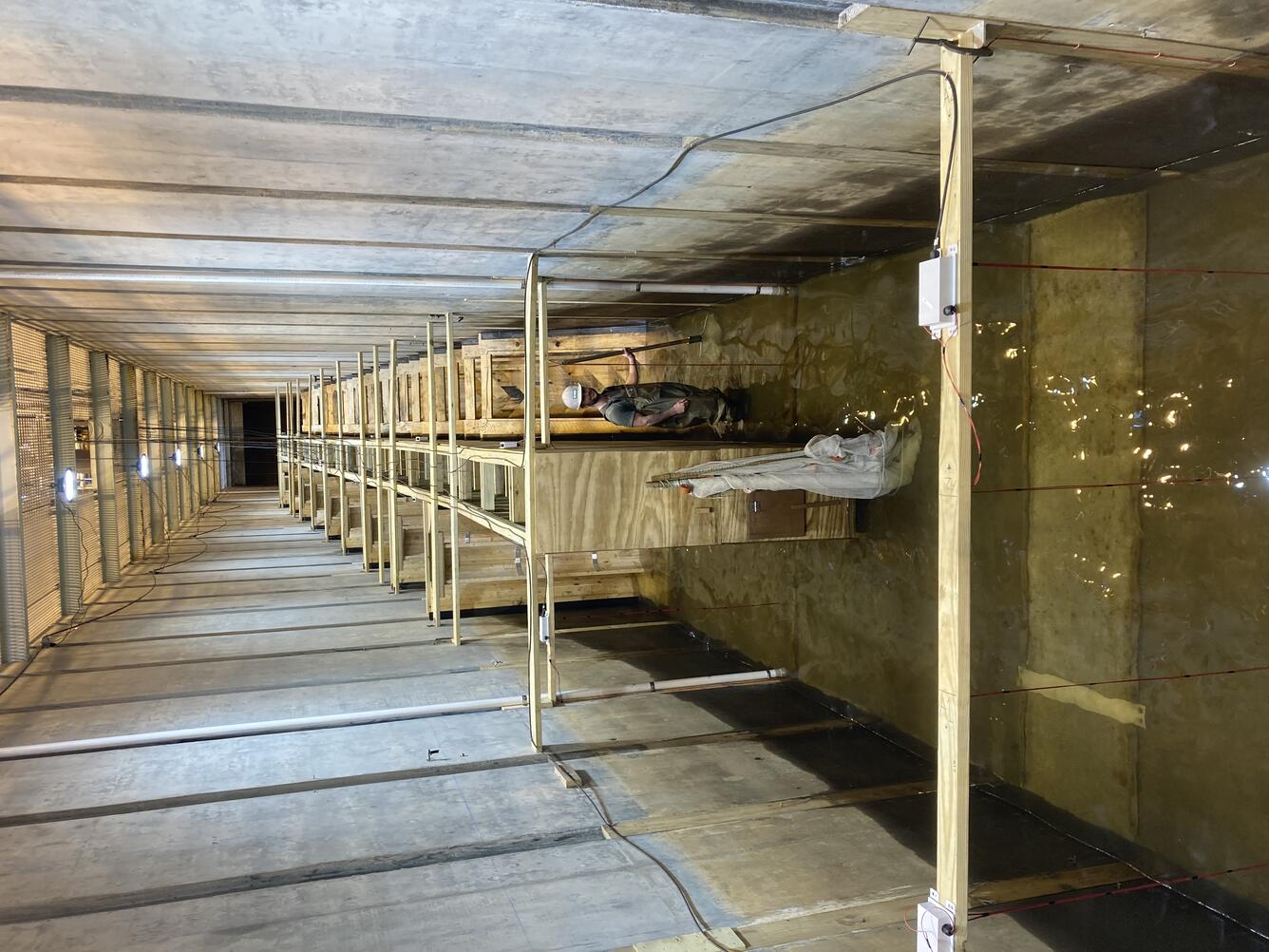 Man stands at the downstream end of a wooden fishway inside a 10-ft wide concrete flume holding a dip net.