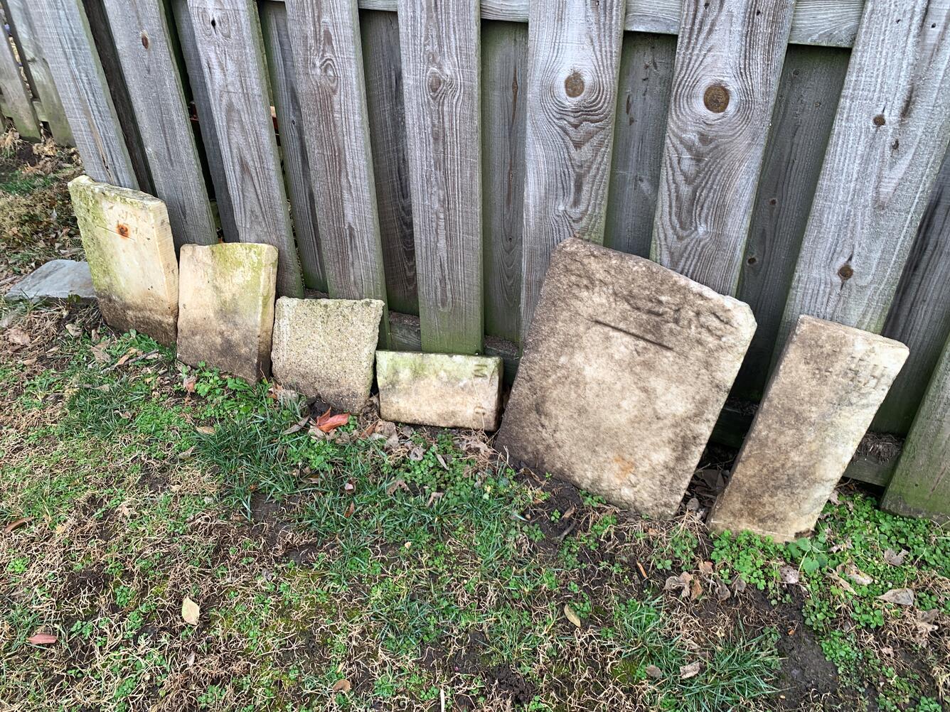 Gravestones leaning against a wooden fence