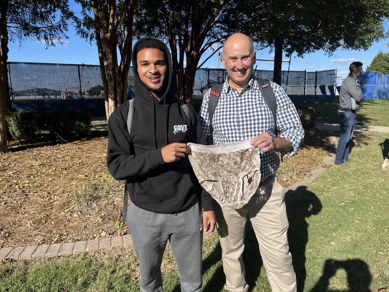 Two people smiling for photo outside holding decomposed clothing