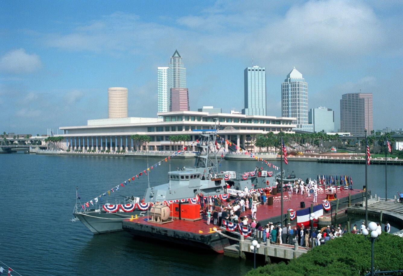 A photograph of a boat with a group of people celebrating onTampa Bay with coastline in view.