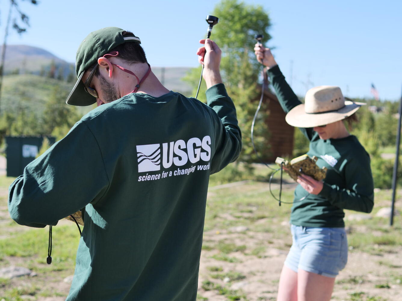 Two scientists wearing USGS shirts hold microphones attached to bat detectors high in the air