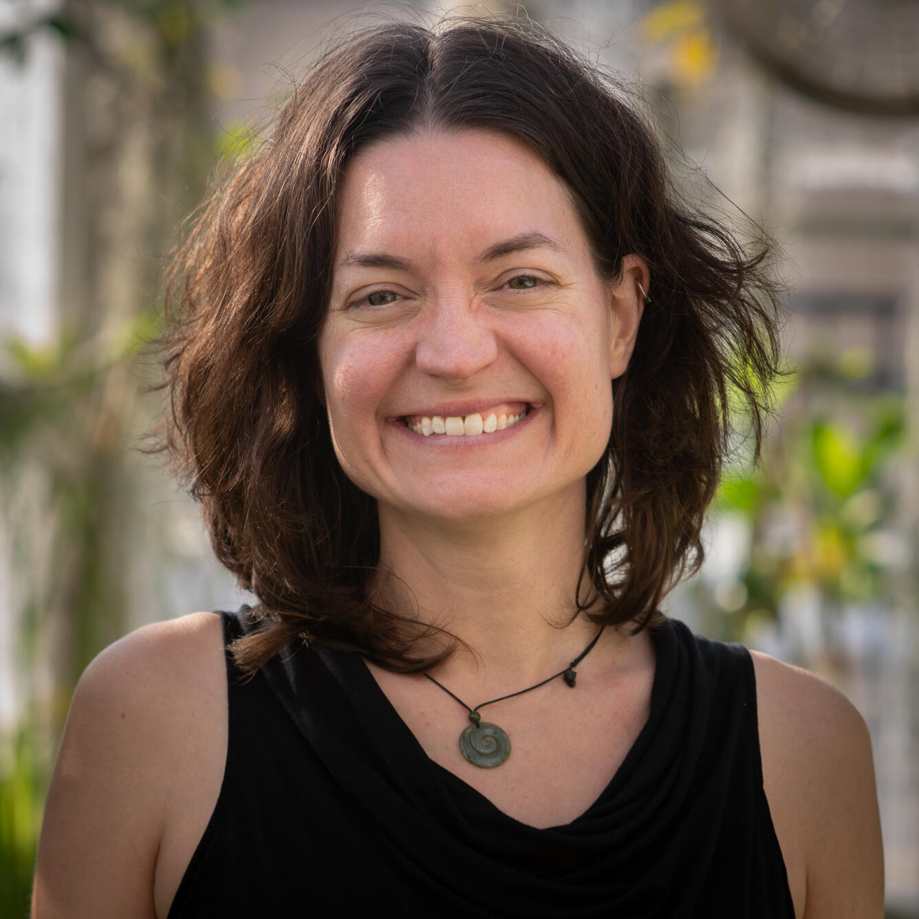 Headshot of a woman with shoulder length dark brown hair and wearing a black tank top stands smiling at the camera.