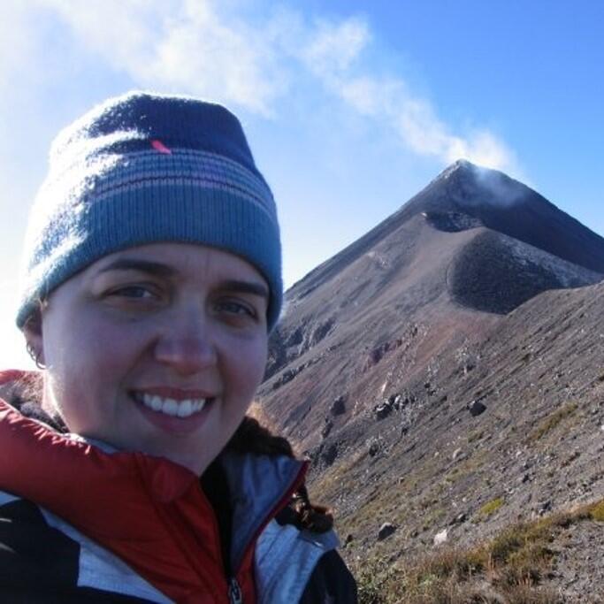 Woman with blue hat standing in front of a steaming volcanic peak