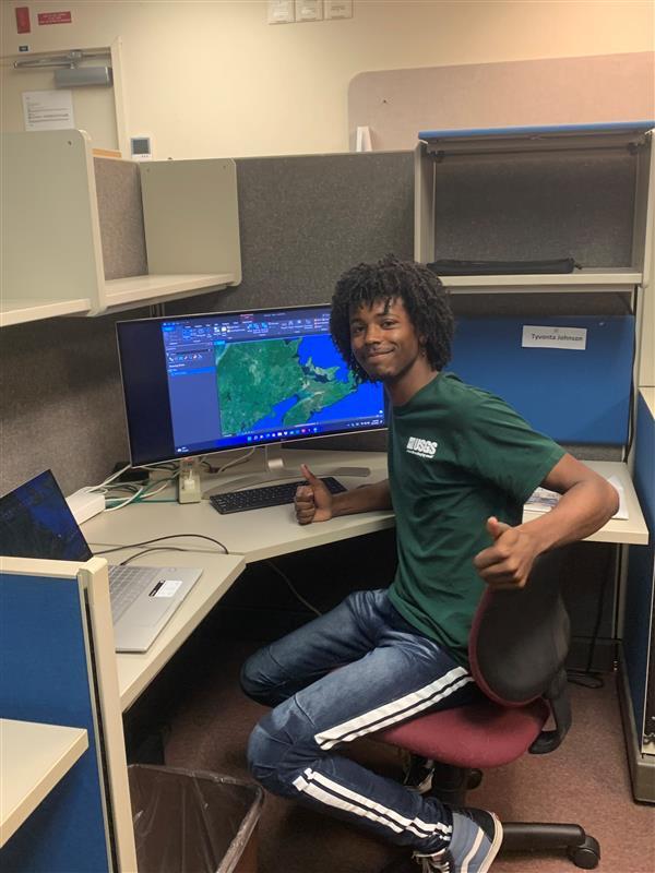 Person sitting at desk with laptop and larger desktop, smiling and giving two thumbs up