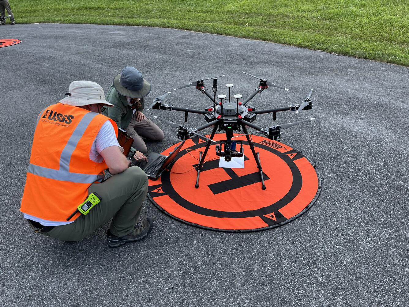 Technicians squat next to drone to evaluate and calibrate it before it takes flight