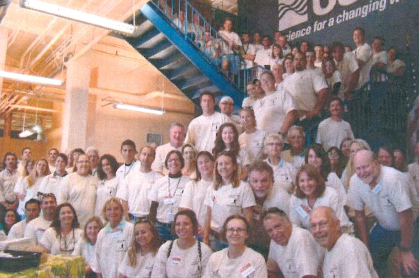 A large group of people in white USGS t-shirts on a blue stairwell smiling