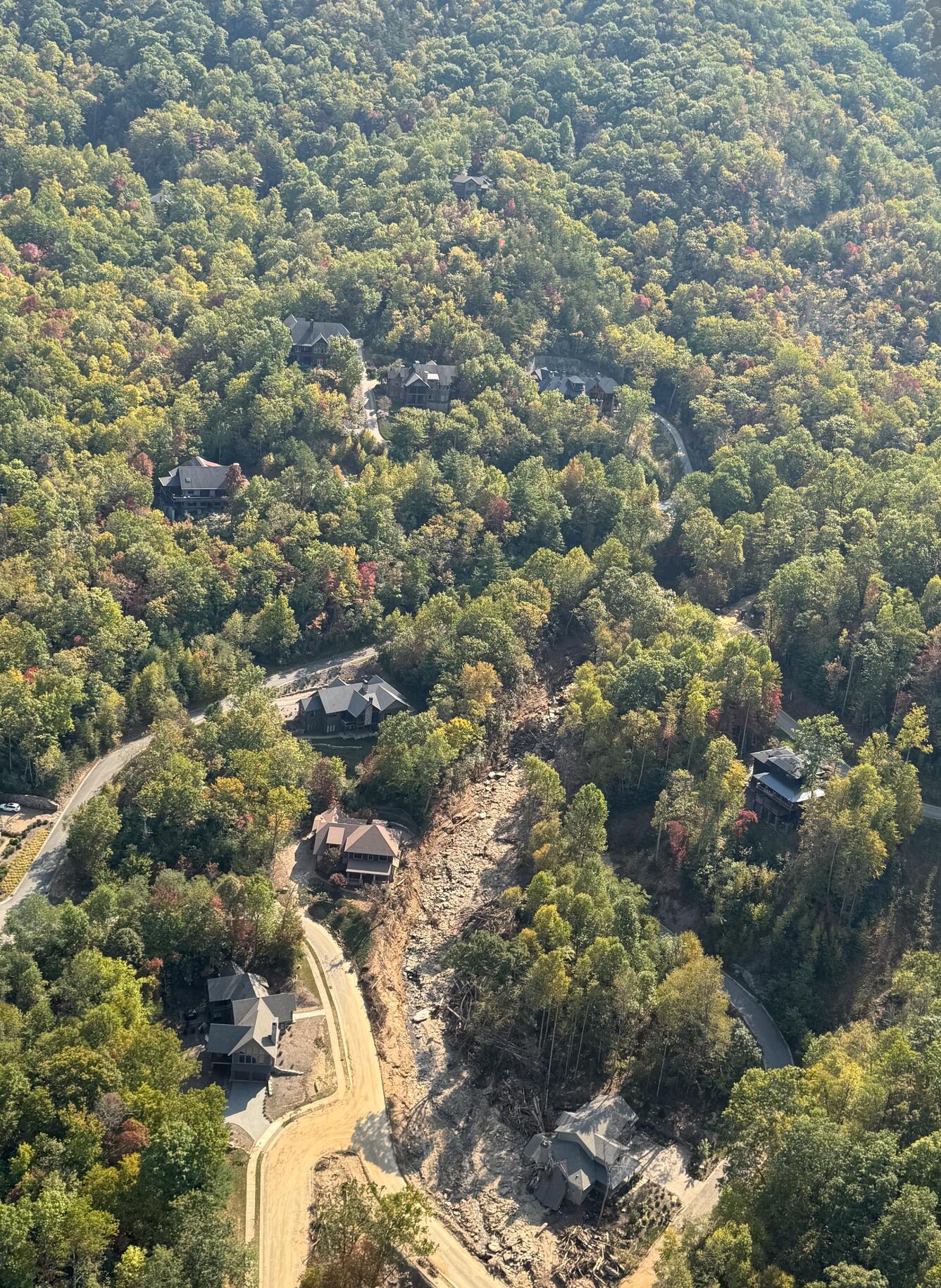 aerial view of forested area with landslide path visible near houses and road