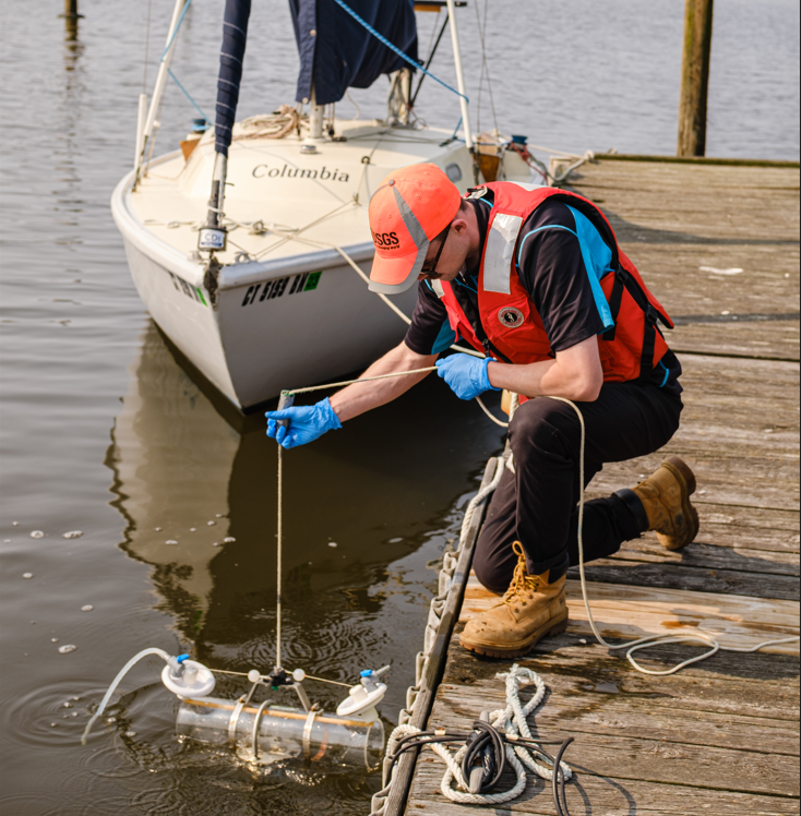 A hydrologic technician drops a water quality sampler into a river from a dock. 