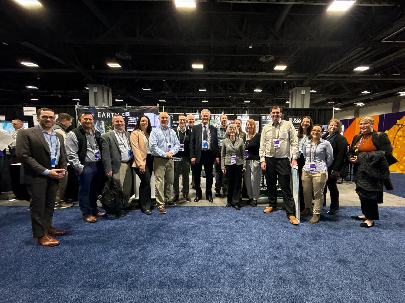 17 people stand in a row at a conference, smiling for the camera