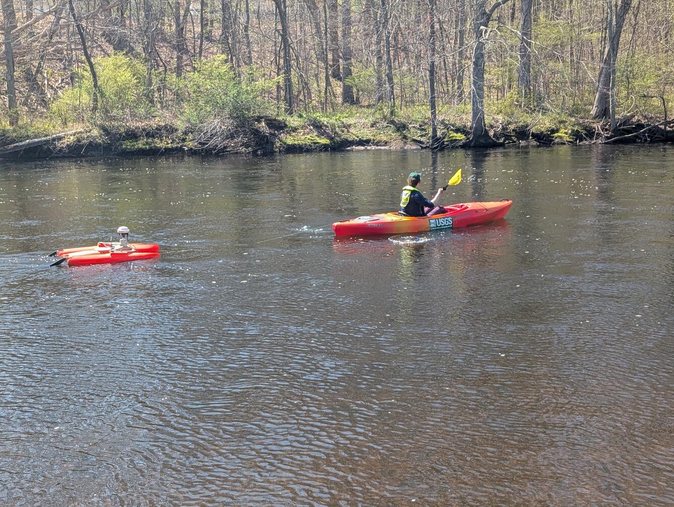 A woman kayaks upstream while towing an orange ADCP behind the kayak. 