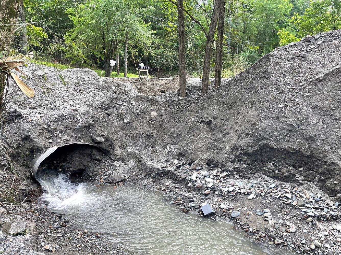 Clogged culvert pipe filled with sediment and some water running out of it.
