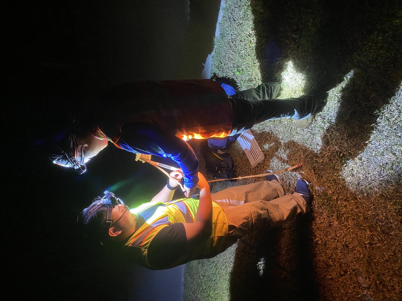 Two people with headlamps use measuring tape with a snake at night.