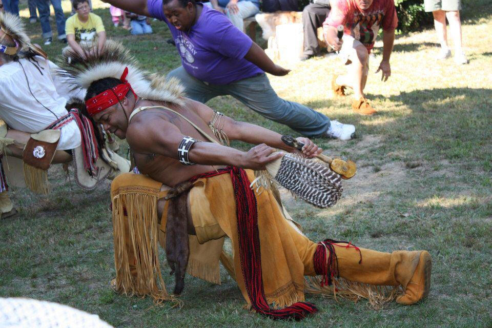 Native American man in Native American clothing kneeling on the ground