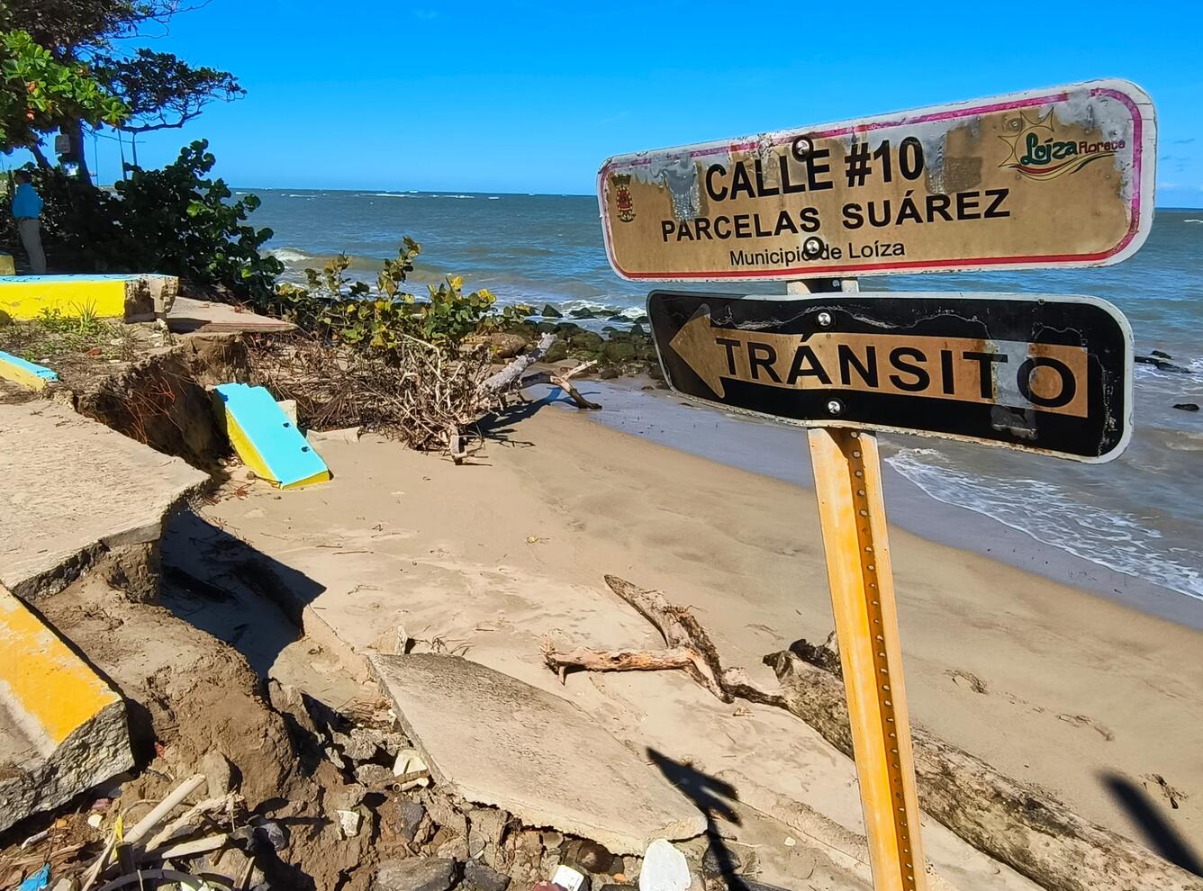 Coastal roadway damaged in Puerto Rico. Two signs in Spanish are shown, Street #10, and a one-way sign.
