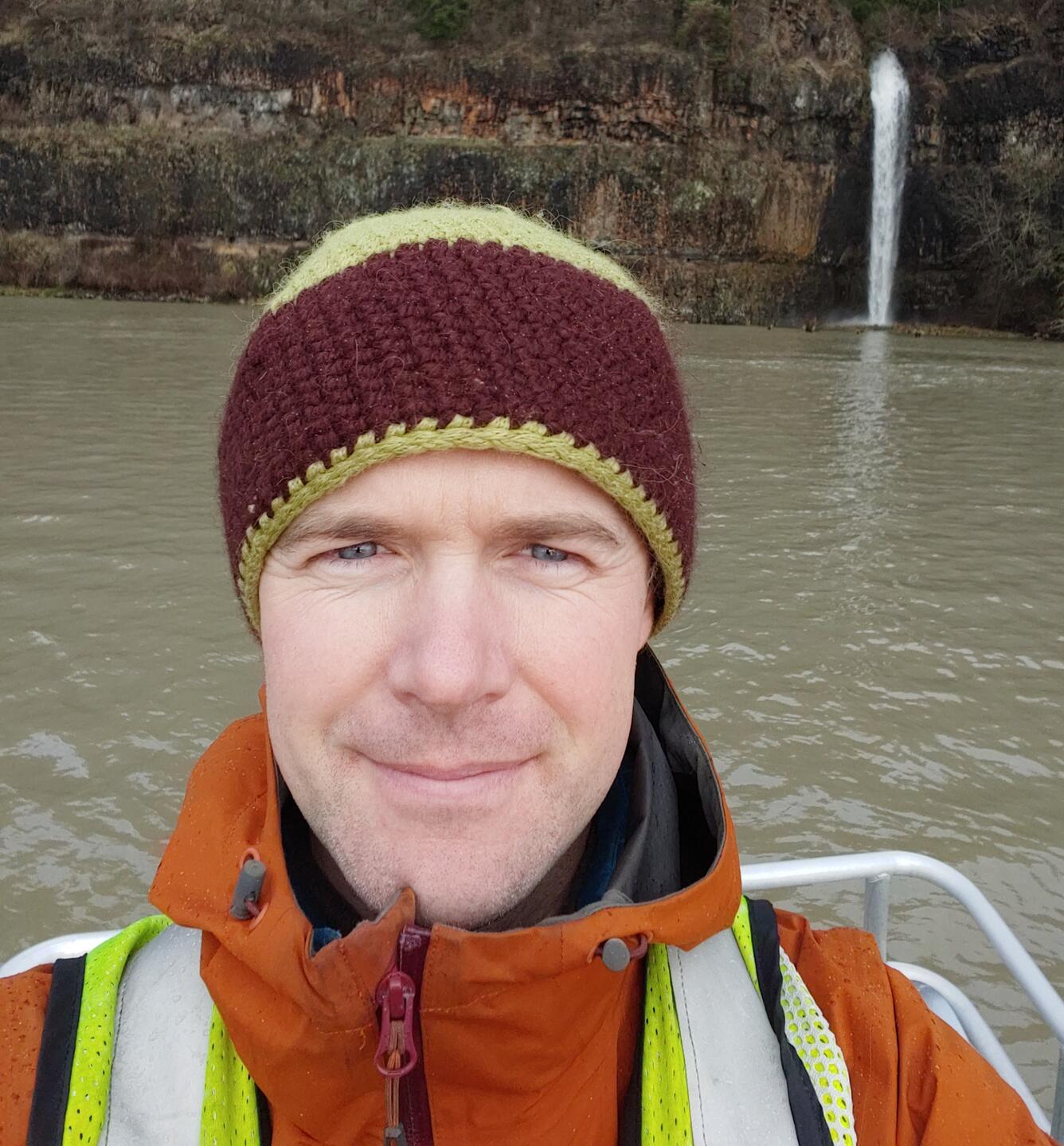 Photo of hydrologist Will Long standing by a river with a waterfall