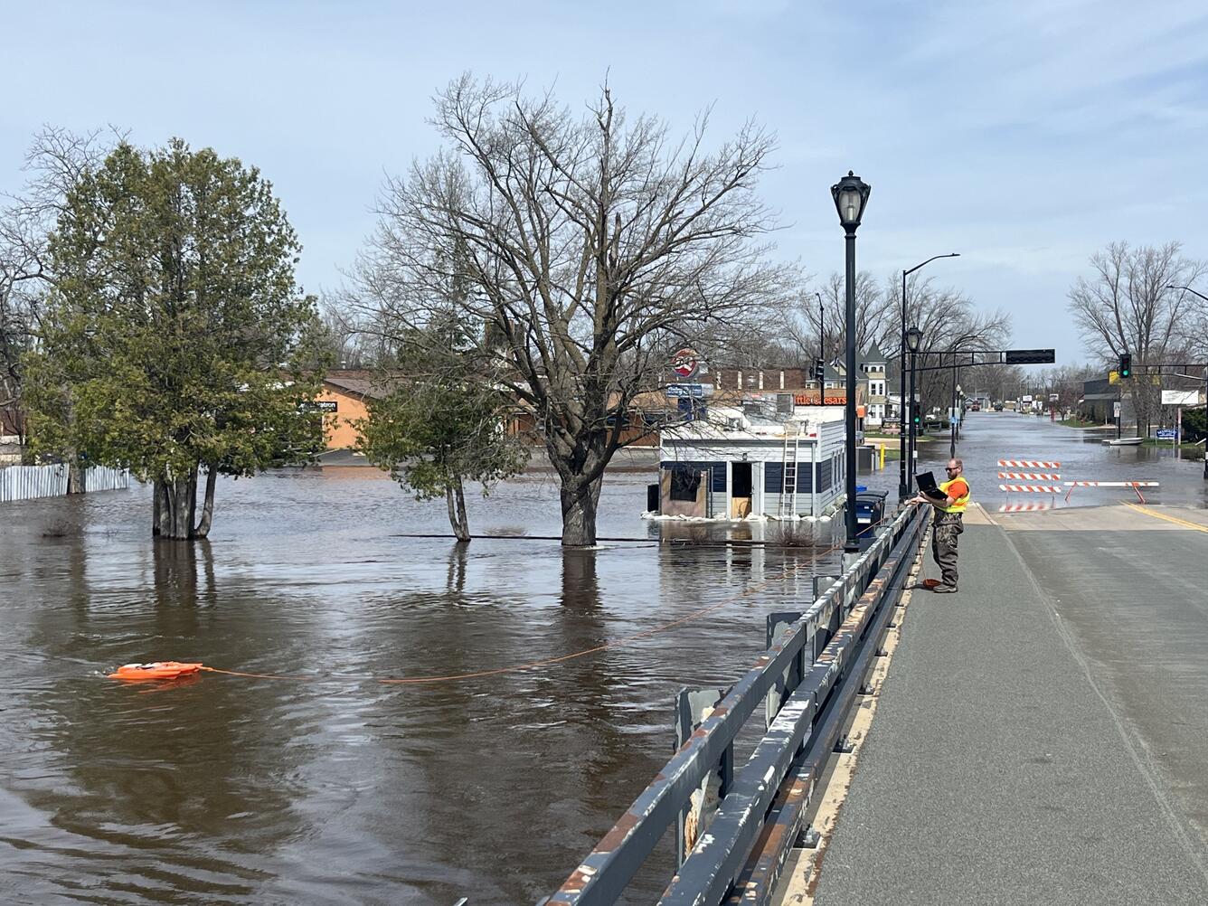 Hydrologic technician takes acoustic Doppler current profiler measurement of flooded river from bridge
