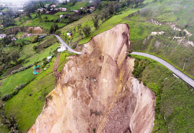 section of grassy hillslope removed and road blocked by large landslide
