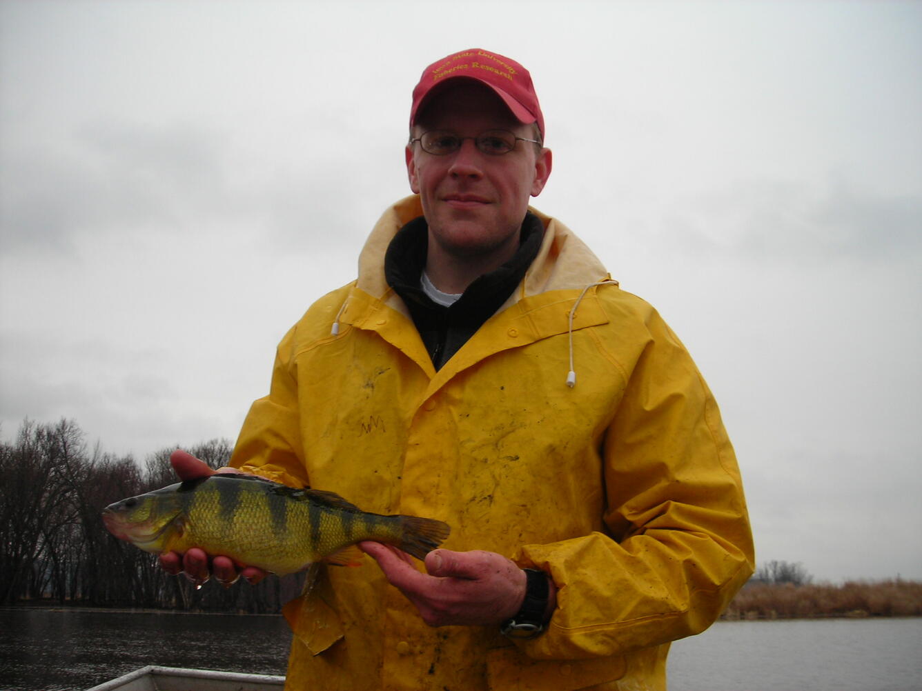 male scientist wearing a yellow raincoat, red hat, and holding a black and yellow fish