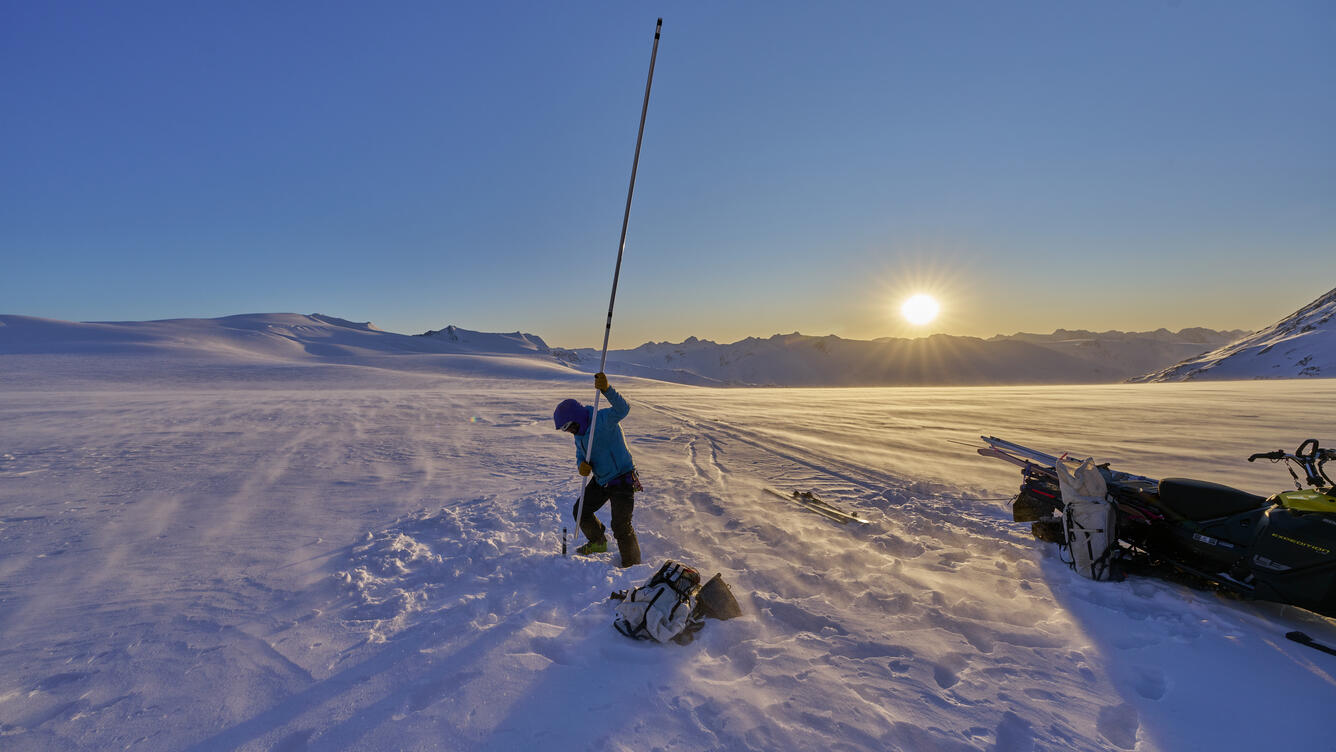 Person holding a lake stake vertically on a glacier.