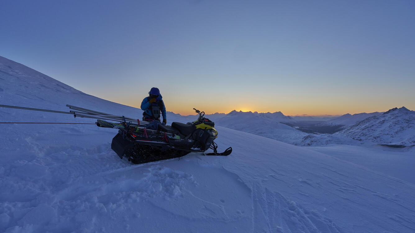 Person standing near a snowmachine on a glacier.