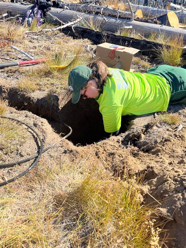Scientist lays on the ground while installing seismic sensor. 