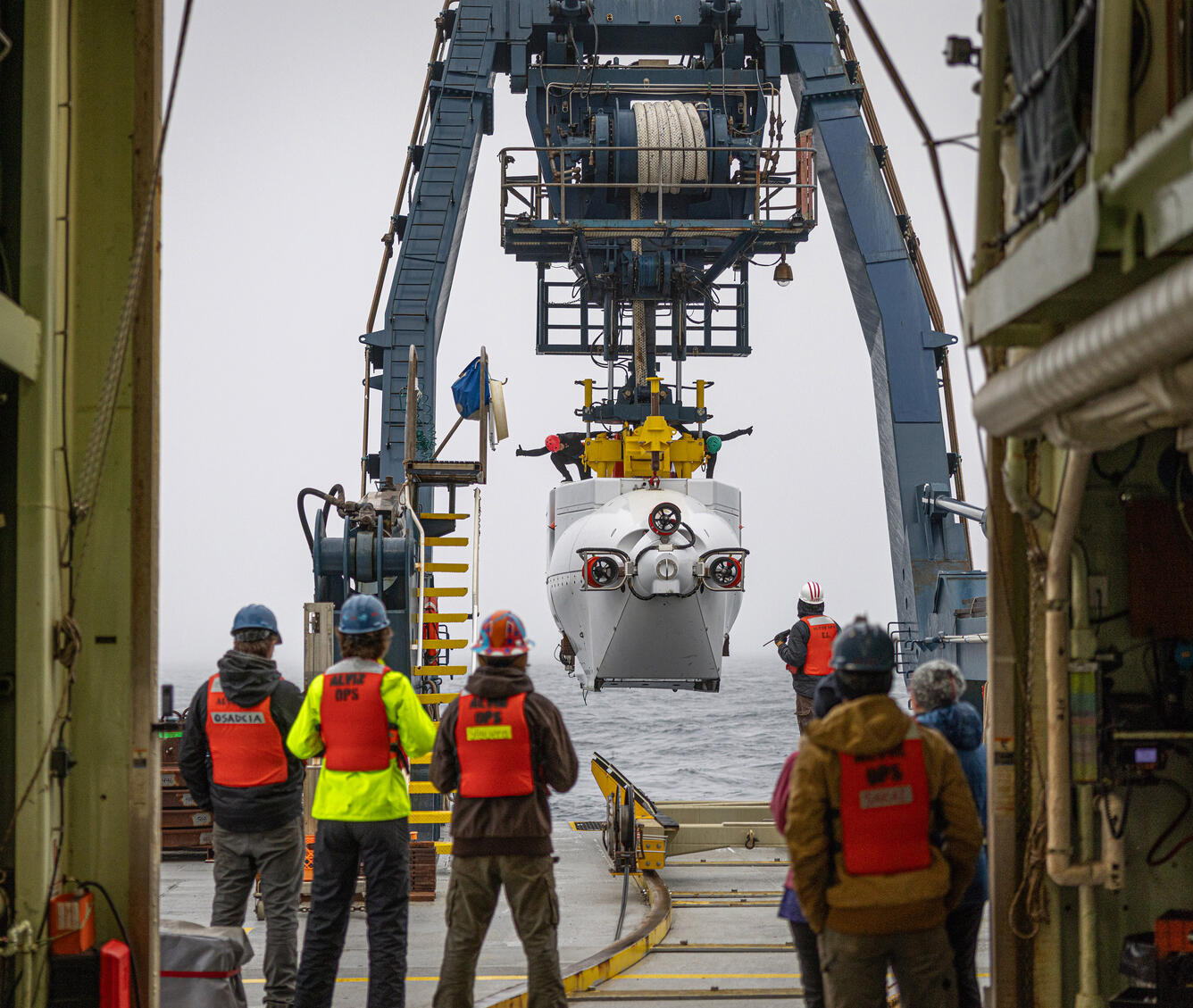 scientists all standing on ship watching equipment get lowered into the water