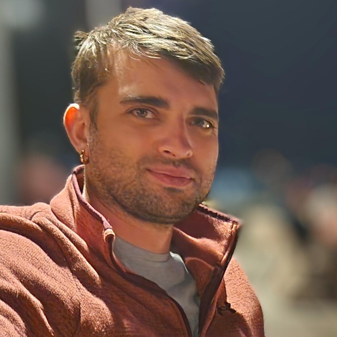 Image of a smiling man in an orange shirt with brown hair