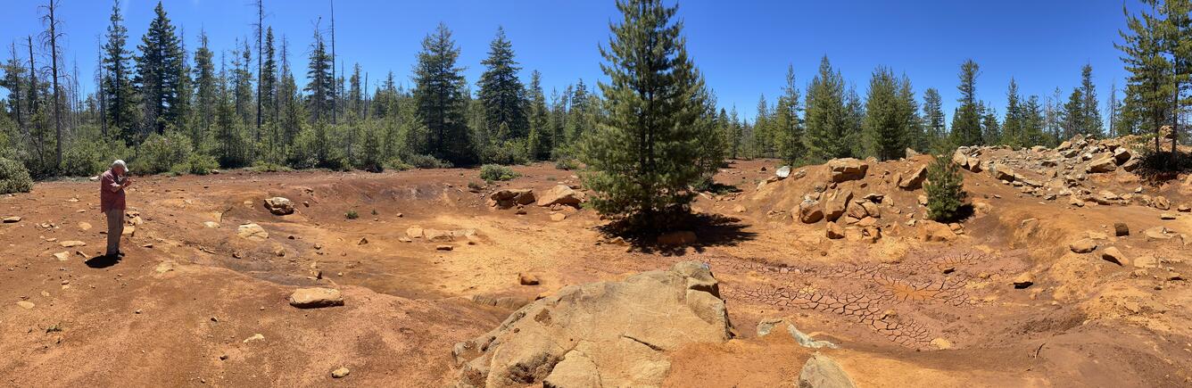 Man standing next to a shallow historic prospecting pit.