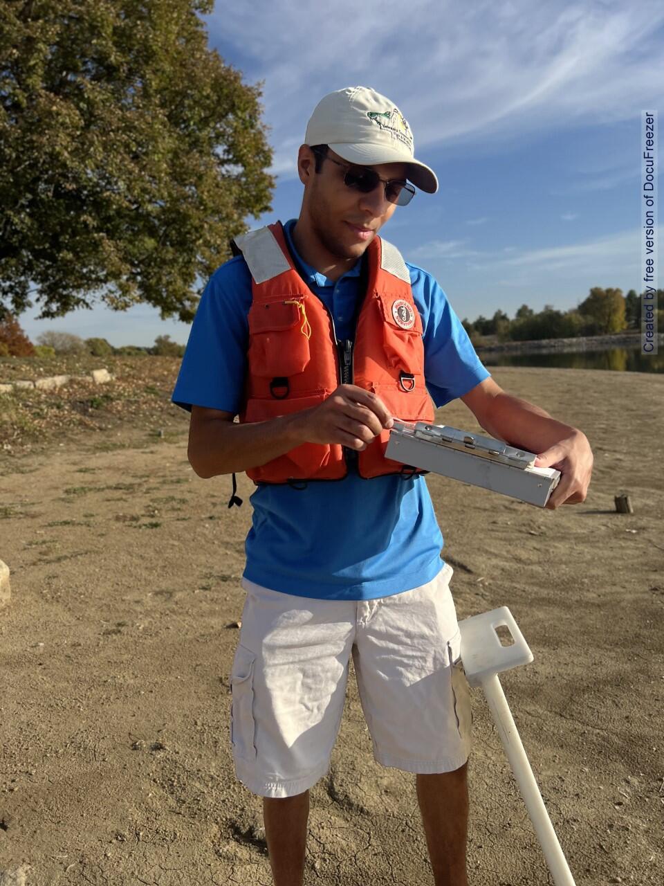 graduate student wearing orange flotation device and blue shirt holding a clip board.