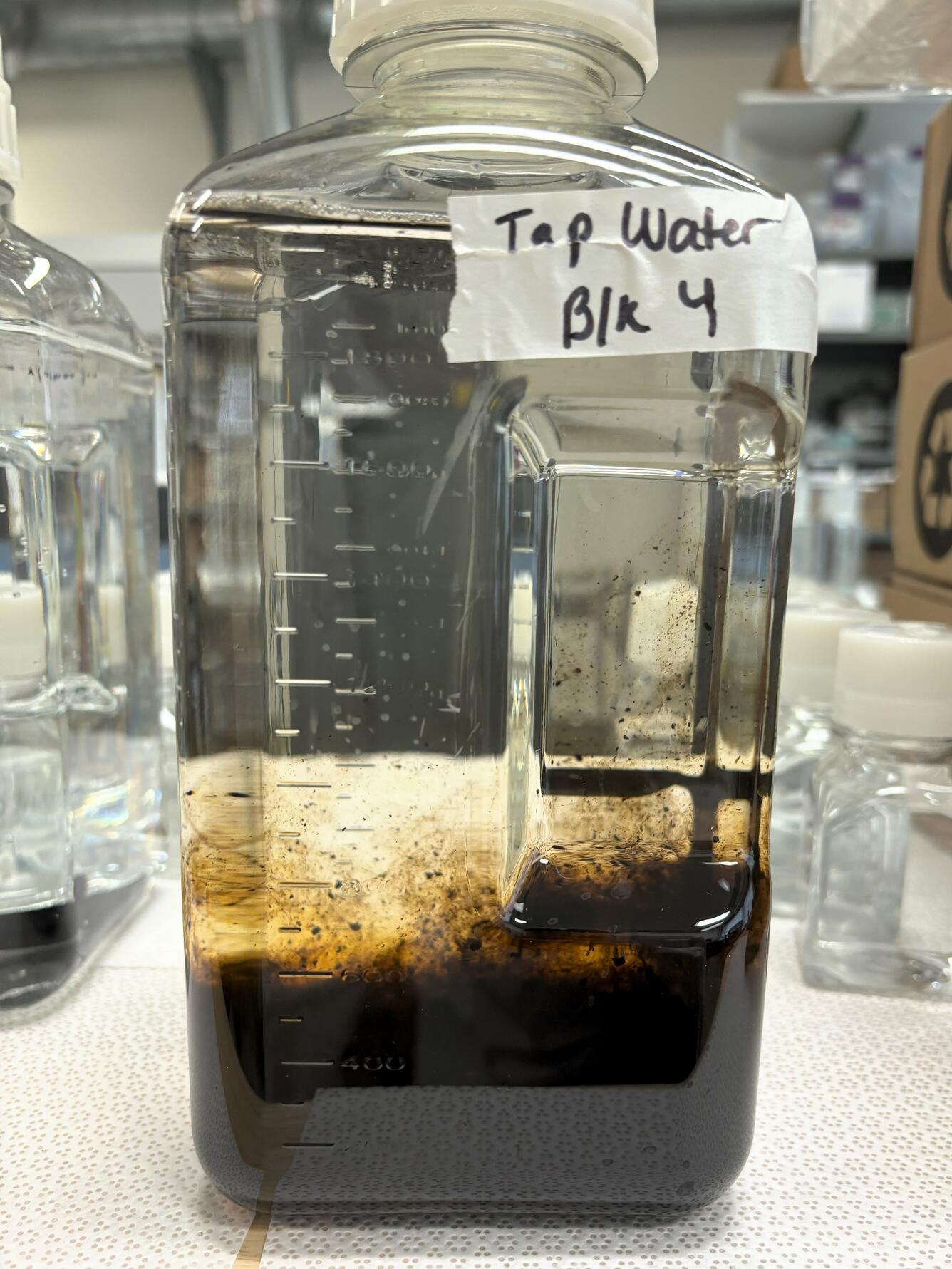 A large plastic sample bottle contains water and brown lignin settling at the bottom
