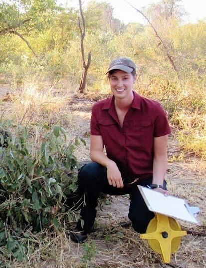 female scientist in the field near green trees wearing a red shirt and hat