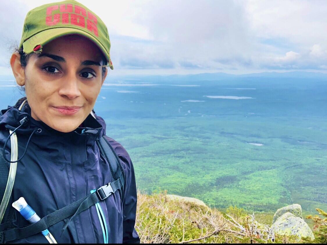 Photo of woman wearing a ballcap, rainjacket, and CamelBak outside